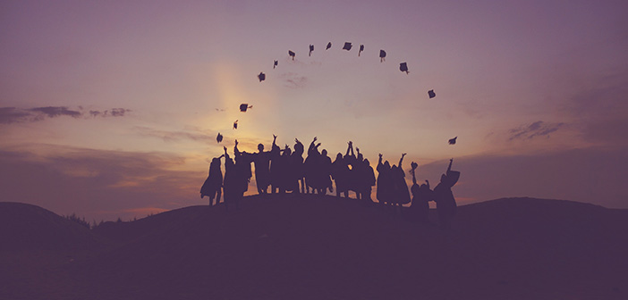 A group of graduates throwing their graduation caps in the air with the sunset in the background