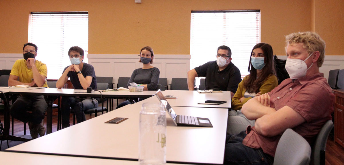 A group of masked visiting scholars sit around a conference table